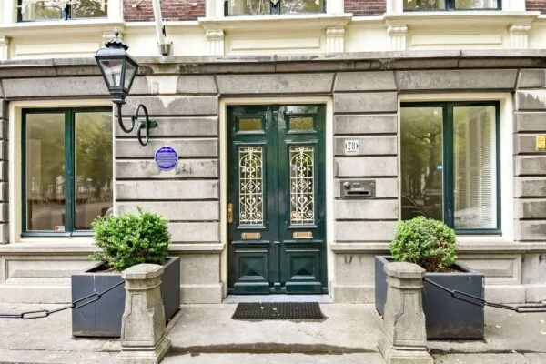 Ingang van een historisch pand aan het Lange Voorhout 28 in Den Haag, met twee sierlijke groene deuren, een blauwe herdenkingsplaquette en symmetrische plantenbakken.